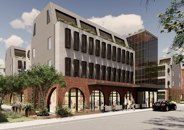 Architectural rendering of a contemporary multi-storey urban mixed-use building. The development combines a red-brick lower level with repeated tall arched shopfront openings, pale vertically ribbed upper facades, projecting dark window surrounds, rooftop planting, and a prominent glazed circulation or lobby volume. Landscaped planters and street frontage are visible, with smaller connected building wings around the main block.