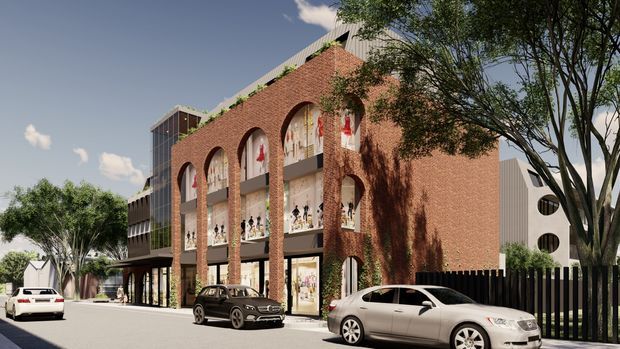 Architectural rendering of a multi-storey urban commercial building with a prominent red brick facade, tall arched openings, glazed shopfronts, balconies or gallery levels, and a contrasting modern side and rear volume. Mature street trees, a black vertical-slat fence, and parked cars frame the streetscape.