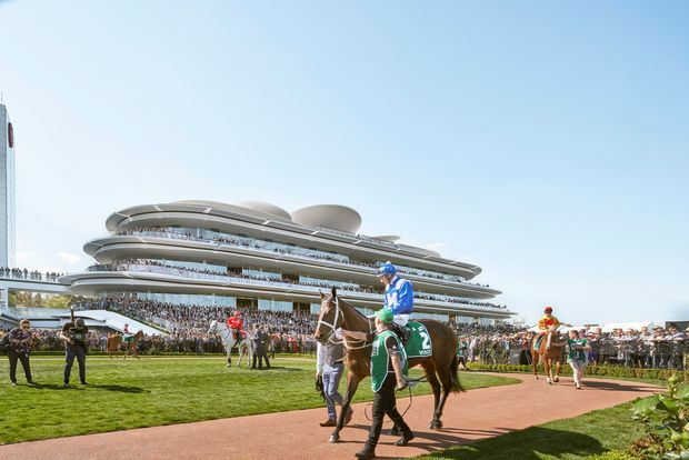 A bright exterior view of a large contemporary multi-level grandstand or racecourse building with sweeping layered terraces, curved roof forms, extensive glazing, and crowded spectator balconies. In the foreground, jockeys and horses move along a paved track beside a manicured lawn. The scene is photographed under a clear blue sky.