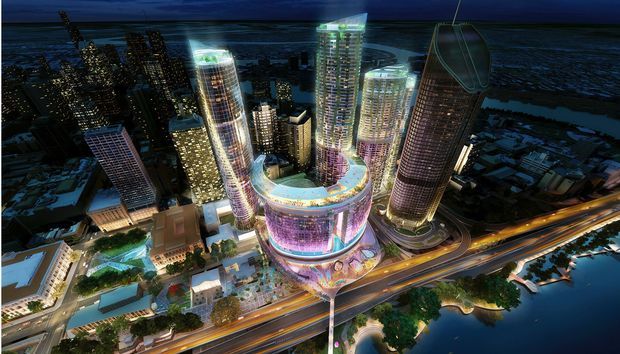 A nighttime aerial architectural rendering of a large urban mixed-use development beside waterways. The scheme is dominated by a glowing circular podium with a ring-shaped roof and multiple illuminated high-rise towers, including cylindrical and curved forms, connected by landscaped public spaces and surrounded by multilane roads.