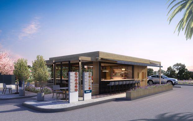 Architectural rendering of a compact contemporary roadside café or service kiosk with a flat, projecting roof, dark structural framing, extensive glazing, timber-toned wall cladding, and a long outdoor-facing counter with bar stools. A paved forecourt includes freestanding menu or signage panels, planters, and outdoor seating, with parked cars visible in the background.