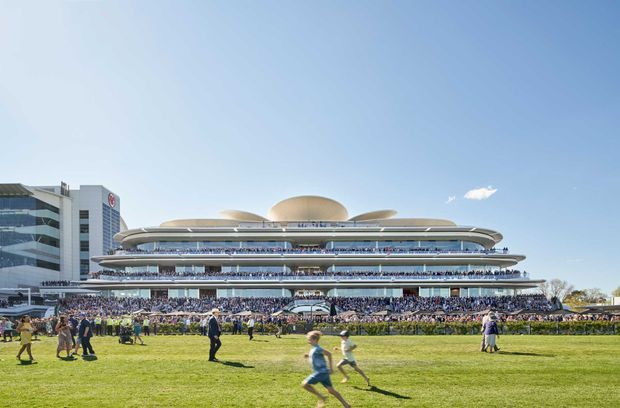Wide exterior view of a large multi-level modern grandstand or events venue across an expansive grass field. The building features sweeping horizontal terraces, extensive glazing, and multiple rounded saucer-like roof forms, with a crowd gathered along the frontage under a clear blue sky.