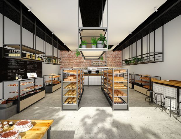 Bright industrial-style bakery or café interior with open shelving, central display racks filled with baked goods, exposed red brick walls, black metal framing, concrete flooring, a service counter at the rear, and hanging planter shelves. A small timber-topped seating area with stools is visible on the right.