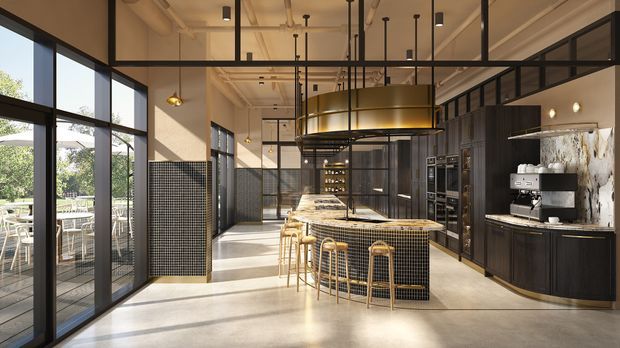 A spacious contemporary kitchen and entertaining area with a large central island, integrated seating, dark timber cabinetry, stone benchtops, and a coffee station. Full-height black-framed glazing opens toward an outdoor dining terrace, while exposed services, pendant lighting, black-framed internal glazing, and tiled feature surfaces create an industrial character. A curved brass-toned feature element and warm timber accents add refinement.