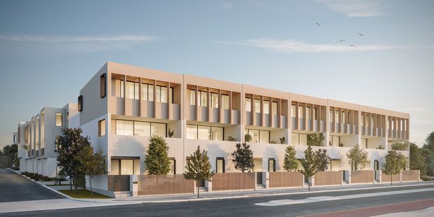 Architectural exterior rendering of a contemporary multi-storey townhouse or apartment development. The elongated building has a stepped massing, pale rendered lower levels, warm vertical timber-toned cladding and screening, repetitive floor-to-ceiling windows, recessed balconies, private fenced ground-level courtyards, and landscaped street frontage. The image is viewed from a broad urban street, with additional building wings extending behind the main facade.