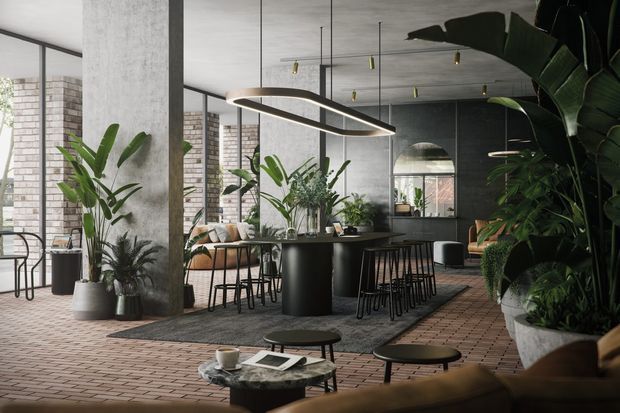 A spacious, plant-filled contemporary interior arranged as a café-style living and dining space. The room features a long dark island or communal table with stools, lounge seating, exposed concrete columns and ceiling, full-height black-framed glazing, brick flooring, and a sculptural linear pendant light. Abundant large indoor plants soften the industrial material palette, while a dark arched opening and reflective surfaces add depth.