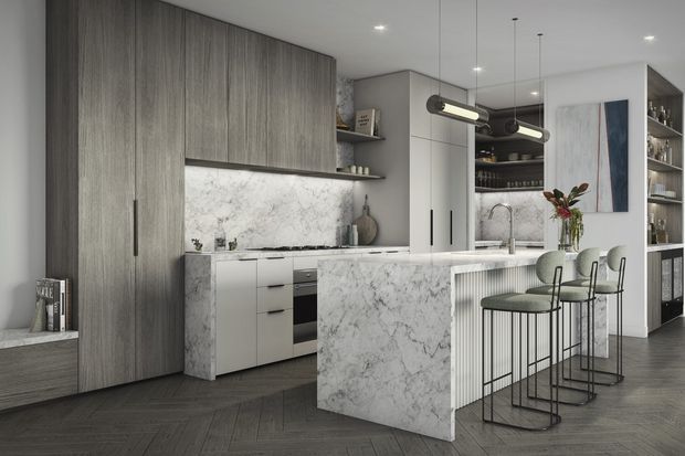 A refined contemporary kitchen with a large marble-clad island, integrated white cabinetry, tall grey wood-grain storage units, open shelving, and three bar stools. Linear pendant lights hang above the island, while dark herringbone flooring and restrained styling create a polished, sophisticated atmosphere.