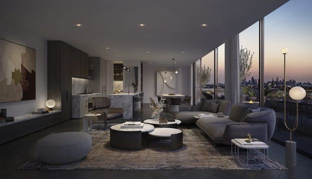 A sophisticated open-plan living room at dusk, with floor-to-ceiling glazing overlooking a city skyline. The room features a large sectional sofa, sculptural lounge chairs and ottomans, layered round coffee tables, a long dark built-in media cabinet, and a compact kitchen or bar area in the background. Recessed ceiling lighting and sculptural floor lamps create a warm, refined atmosphere, while dark timber-toned joinery, neutral furnishings, and a textured rug give the space a contemporary luxurious feel.