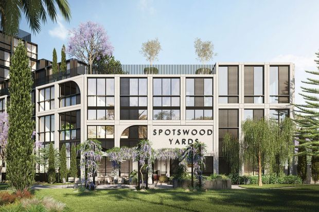 Architectural rendering of a contemporary multi-storey mixed-use or commercial development named “Spotswood Yards.” The building has a rectilinear glazed facade with dark metal framing, pale concrete or masonry panels, a rooftop terrace with vertical railings and trees, arched openings at ground level, and extensive landscaped planting in the foreground and around the entrance.