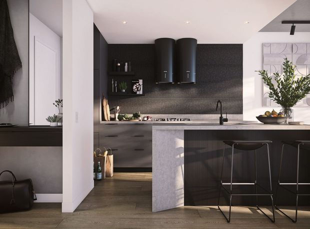 Contemporary kitchen with a dark ribbed feature wall, matte black cylindrical rangehoods, dark timber cabinetry, and a large pale stone island with integrated seating. White walls and ceiling create contrast, while black bar stools, a black tap, open shelving, and restrained greenery add a refined monochrome look. A small adjacent entry or hallway area is visible at left.