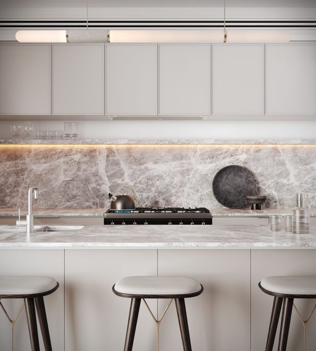 A refined contemporary kitchen with a long island and integrated cooktop, pale grey handleless cabinetry, a dramatic veined stone splashback and matching benchtop, and warm concealed under-cabinet lighting. Three upholstered stools with dark timber or metal legs sit at the island. Linear pendant lighting and brushed metal fixtures add a polished, minimalist feel.