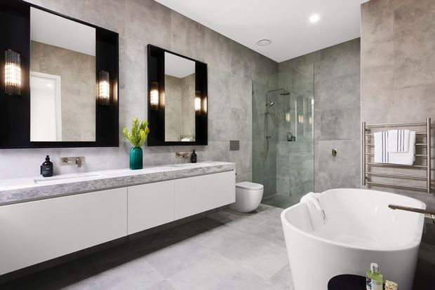 Contemporary bathroom with a long floating double vanity, white cabinetry, grey stone-look benchtop, large black-framed mirrors, textured grey wall finishes, a frameless glass shower, wall-hung toilet, heated towel rail and freestanding white bathtub. The room is bright, refined and spa-like.