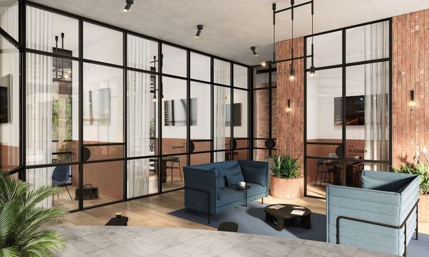 Contemporary commercial lounge or reception area with black-framed glass partitions, exposed red-brick feature walls, pale timber flooring, and modern blue upholstered seating. Pendant lights, indoor plants, and adjacent glazed workspaces create an open-plan office or hospitality setting with an industrial-inspired fit-out.