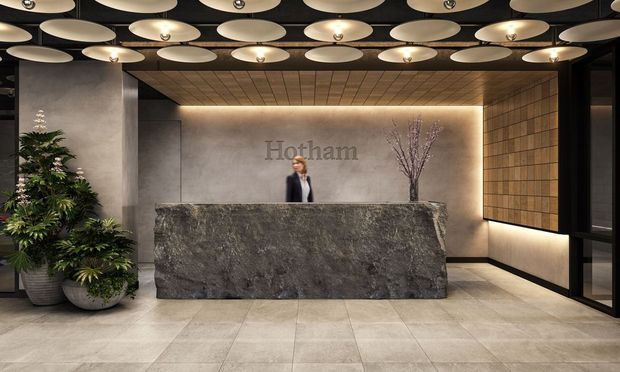 A sophisticated commercial reception lobby featuring a large dark natural-stone reception desk, warm backlit signage wall, timber-look wall panelling, pale tiled flooring, black-framed glazing, indoor plants, and a dramatic ceiling installation of overlapping circular disc lights.