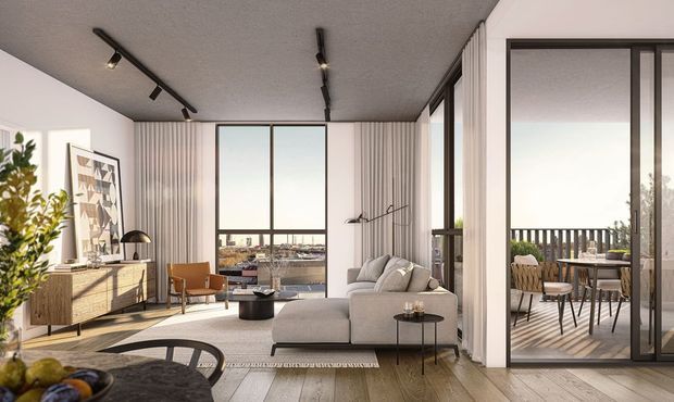 Contemporary open-plan living room with a neutral sectional sofa, timber flooring, a mid-century-inspired sideboard and lounge chair, track lighting, full-height curtains, and expansive black-framed glazing. A dining area and balcony or terrace are visible through the glass doors, with an urban view beyond.