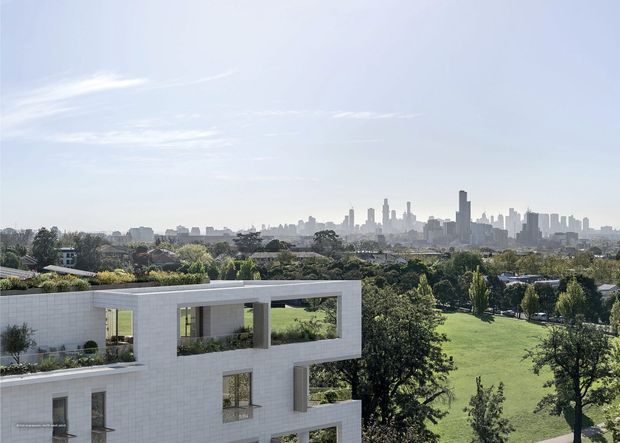 Exterior architectural view of a contemporary white-brick multi-storey residence with large rectangular openings, recessed balconies, and planted roof terraces. The building overlooks a broad green park and landscaped suburban setting, with a dense urban skyline visible in the distance.
