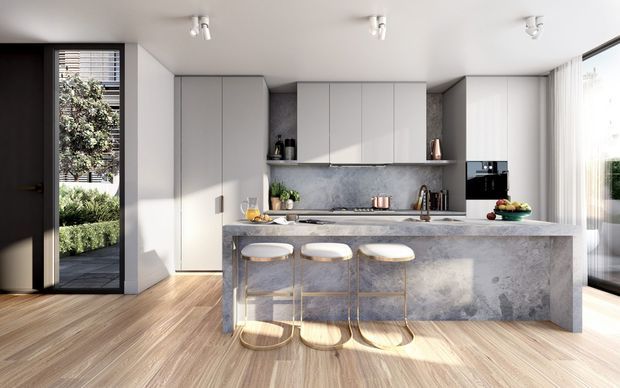A bright contemporary kitchen with a large stone island and three bar stools, full-height pale cabinetry, a matching stone splashback and integrated appliances. Warm timber flooring contrasts with the cool grey finishes, while a glazed garden-facing door and large windows provide natural light.