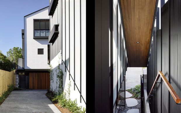 Split architectural exterior view showing a narrow residential driveway and garage entrance on the left, alongside a covered side passage with dark vertical cladding, timber-lined ceiling, glazing, and a timber handrail on the right. The house presents a crisp contemporary facade with white textured masonry, black and white vertical cladding, timber garage doors, and landscaped stepping stones.