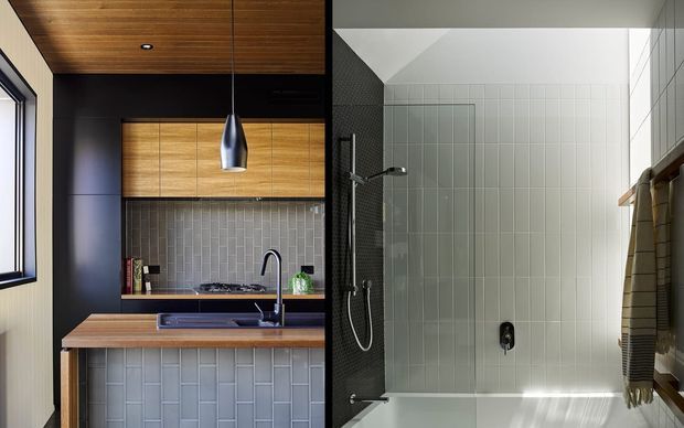 Split image showing a compact kitchen on the left and a contemporary tiled bathroom with shower and bathtub on the right. The kitchen features dark cabinetry, warm timber cabinetry and ceiling, a timber benchtop, grey vertical subway-tile splashback, and a pendant light. The bathroom has pale grid-pattern wall tiles, a dark tiled shower wall, a frameless glass shower screen, and a white bath with timber towel storage.