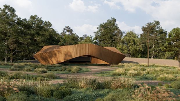 A low, sculptural building set within a naturalistic landscaped site. The structure has a sweeping, organically curved form clad in warm vertical timber boards, with a dark recessed entrance or opening beneath the central arch. Gravel paths and ornamental grasses surround the building, with mature woodland forming the background.