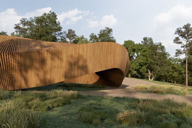 A sculptural contemporary building set within a landscaped outdoor site. The elongated, organically curved form is wrapped in closely spaced vertical timber-like ribs, creating a warm brown textured facade. A dramatic recessed opening forms a sheltered passage or entrance beneath the sweeping volume. Native-style grasses and planted garden beds surround the structure, with mature trees visible behind it under a partly cloudy sky.