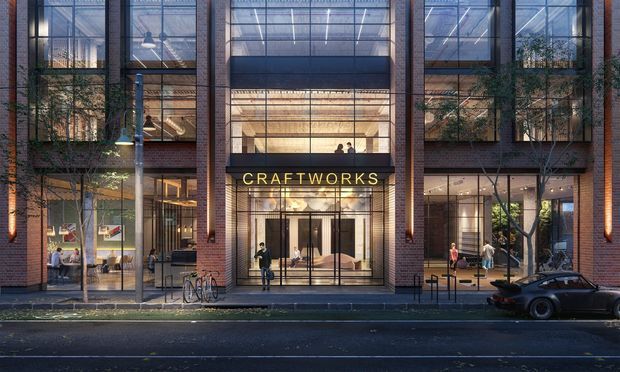 Street-level architectural rendering of a contemporary multi-storey commercial building with a transparent glazed facade, exposed red-brown brick piers, and a prominent illuminated CRAFTWORKS entrance sign. The ground floor contains retail or hospitality-style interiors visible through the glazing, while upper levels show large glass panels, interior lighting, and planted trees. Urban streetscape with pedestrians, bicycles, and a parked car in the foreground.