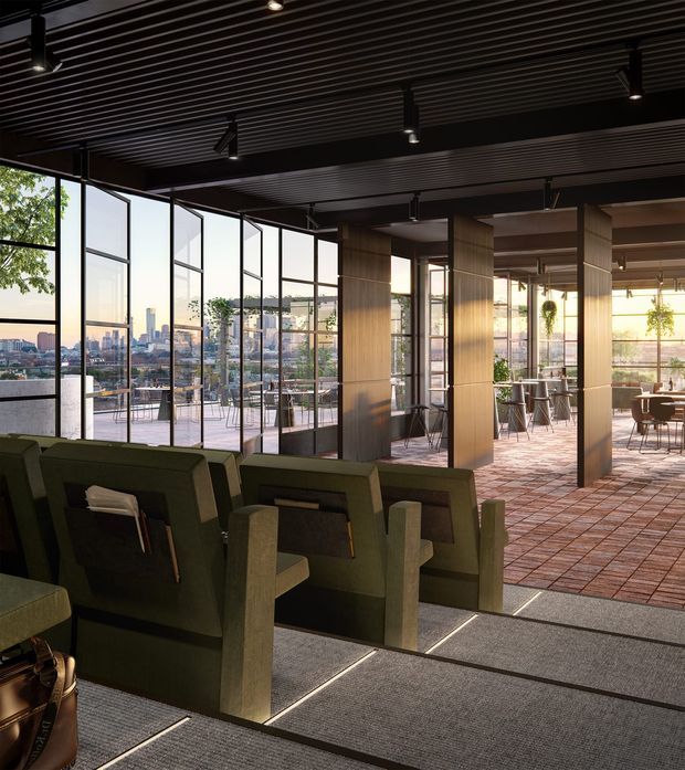 A sophisticated rooftop hospitality lounge or commercial interior with floor-to-ceiling glazing overlooking a dense city skyline. The foreground contains rows of deep green upholstered lounge chairs on dark carpet, while the adjoining terrace or dining area features exposed brick-look flooring, timber-clad structural columns, café tables and stools. A dark linear slatted ceiling with track lighting creates a refined, moody atmosphere, with warm sunlight entering through the glazed facade.