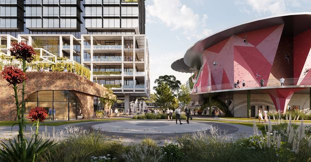 Architectural visualization of a contemporary mixed-use urban precinct, featuring a tall apartment or commercial building on the left and a distinctive sculptural, curved-roof pavilion on the right with a faceted pink geometric facade. Landscaped public space, pedestrian paths, planting, and an open plaza connect the buildings.
