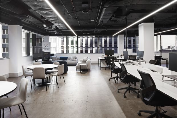 Open-plan contemporary office interior with shared workstations, black ergonomic chairs, meeting tables, lounge seating, exposed services, linear LED lighting, concrete flooring, and extensive interior glazing.