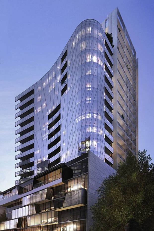 A tall contemporary urban tower photographed at dusk, with a dramatic curved glass curtain-wall facade, visible interior lighting, projecting balconies, and a contrasting rectilinear concrete or stone-clad vertical wing. The lower levels feature layered terraces and extensive glazing, with trees partially obscuring the base.