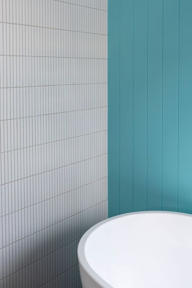 Close-up architectural detail of a contemporary bathroom corner, featuring a white freestanding bathtub, a pale grey vertically ribbed tiled wall, and a vivid turquoise-blue vertical wall panel.