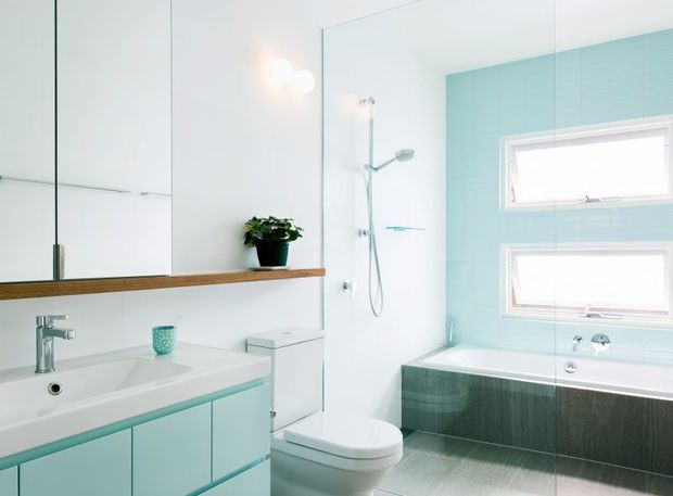 Bright contemporary bathroom with a pale aqua built-in vanity, white basin, wall-mounted mirror cabinetry, timber shelf, toilet, open shower, and a full-size bathtub. Aqua tiled walls and dark textured bath surround create a fresh, clean palette, with high-level horizontal windows providing natural light.