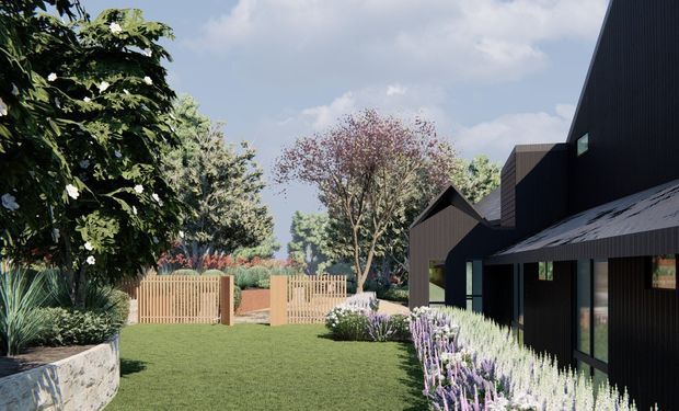 Exterior architectural view of a dark-clad contemporary house with angular gabled roof forms, extensive vertical cladding, and landscaped garden surrounds. A lawn, timber fencing and gates, mature planting, and lavender-like border planting frame the building.