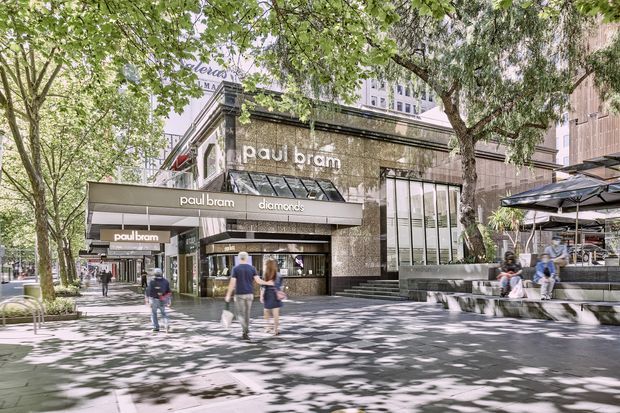 Street-level view of a contemporary Paul Bram diamonds jewellery store in an urban retail setting. The shop has a dark stone or tile facade, large glazed display windows, projecting branded awnings, and a prominent entrance. Mature street trees, paved sidewalks, outdoor seating, and surrounding multi-storey buildings frame the commercial frontage.