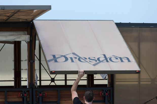Exterior close-up of a branded mobile display or transport structure, with a large raised white panel bearing the word “Presden,” dark metal framing, translucent panels, and timber-toned sections. A person is operating the panel mechanism. The image is primarily about the exterior structure rather than an identifiable room or interior space.