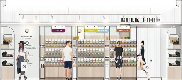 A bright retail bulk-food store interior with floor-to-ceiling wall shelving filled with labelled jars and packaged goods. Large black “BULK FOOD” lettering is mounted above the displays, with category signs, integrated shelving, and product dispensers. Customers and branded merchandise are visible, while the fixed fit-out is predominantly white and light timber with black detailing.