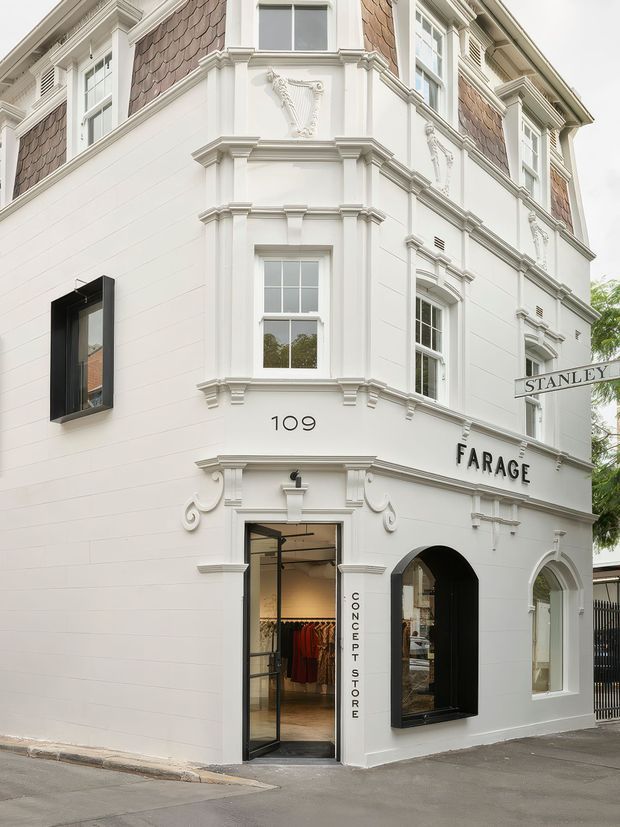 Street-level view of a refined historic-style commercial shopfront at 109 Farage, featuring a white rendered facade, ornate classical mouldings, decorative relief panels, bay-window detailing, arched openings, and dark-framed display windows. The ground floor is a concept clothing store, while the upper level has traditional shingle-clad sections and multi-pane sash-style windows.