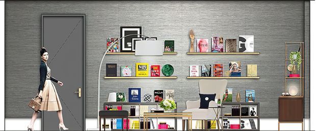 A stylised contemporary retail or showroom interior with a dark grey textured feature wall, a single dark door, and extensive open shelving displaying books, magazines, framed graphics, and decorative objects. A seated lounge chair, small table with flowers, shelving, and a timber-toned side cabinet complete the composition. The image appears to be a designed commercial display space, with a fashion mannequin or cutout figure positioned near the doorway.