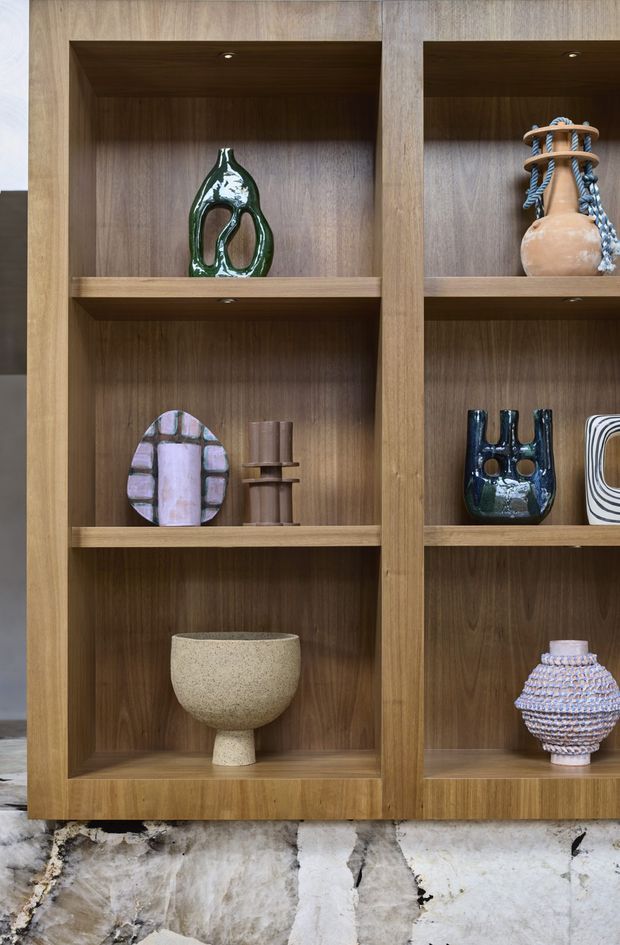 Close-up of a built-in timber display shelving unit with multiple recessed compartments, integrated downlights, and curated decorative vessels. The shelving is set against a dramatic veined natural stone wall or base, creating a warm, refined interior feature.
