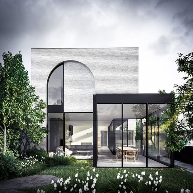 Contemporary two-storey residence with a pale textured masonry facade, a tall arched window, and a dark-framed glazed extension. The transparent living and dining areas open toward a landscaped garden with dense planting and white flowers.