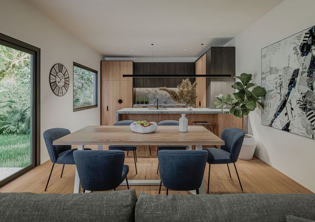 A contemporary open-plan dining and kitchen area viewed from behind a sofa. A rectangular timber dining table with six upholstered navy chairs occupies the foreground, while a compact kitchen features dark timber cabinetry, a light benchtop, integrated appliances, and open shelving. Full-height glazing and a framed window bring in garden views, with warm timber flooring, neutral walls, greenery, and abstract wall art completing the space.