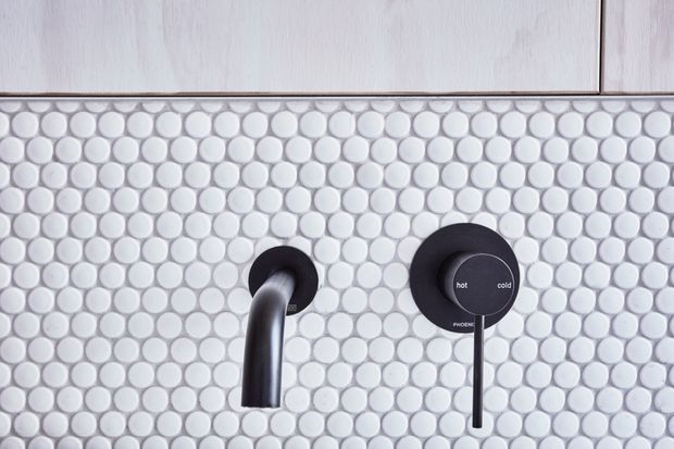 Close-up of a contemporary bathroom shower wall featuring small round white mosaic tiles, pale timber-look cabinetry above, and matte black wall-mounted shower controls and spout.