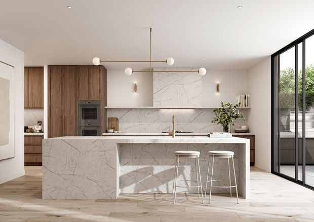 A bright, refined contemporary kitchen with a large veined stone island, integrated timber cabinetry, a matching stone splashback, slim brass-toned pendant lighting, and two bar stools. Full-height black-framed glazing opens to an outdoor area, while pale timber flooring and neutral finishes create an airy open-plan setting.