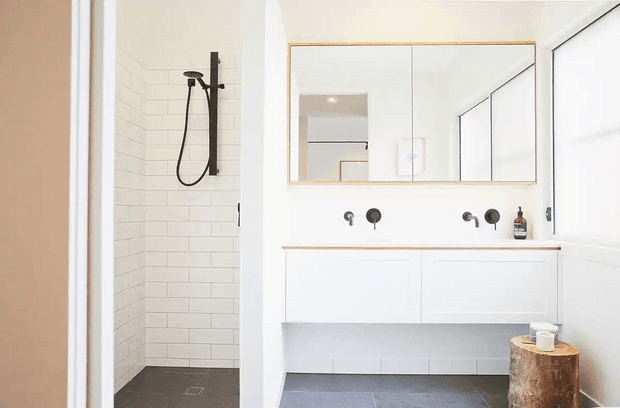 Bright contemporary bathroom with a walk-in shower, white horizontal wall tiles, a dark grey tiled floor, a floating white double vanity, large mirrored cabinetry, and matte black shower and tapware. A timber stump stool adds a natural accent.