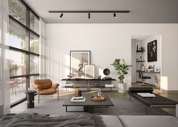 A bright, contemporary open-plan living room with floor-to-ceiling black-framed glazing along one side, a neutral palette, and a dark ceiling-mounted track light. The room contains a low black coffee table, slim media console, sculptural lounge chairs, a tufted daybed, indoor plants, and framed artwork. An open doorway reveals a compact home office with shelving and a desk.