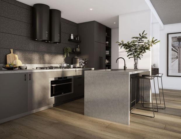 A contemporary open-plan kitchen with dark charcoal cabinetry, a textured dark tiled splashback, pale stone benchtops, integrated black appliances, and a large waterfall-edge island with bar seating. Warm timber flooring contrasts with the monochromatic joinery, while white walls and indoor greenery add brightness. The kitchen includes a sculptural black rangehood, gas cooktop, sink, open shelving, and adjacent dining or living space.