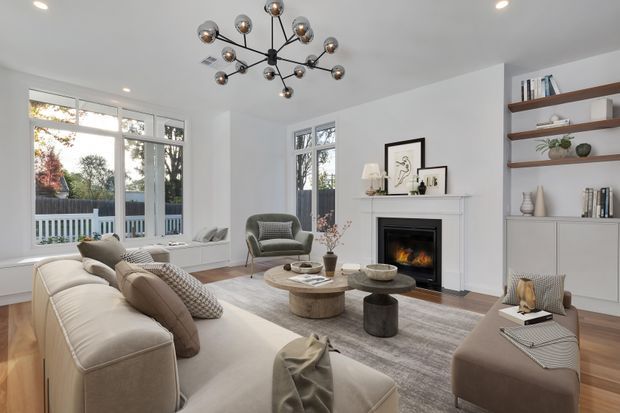 Bright, refined living room with a large cream sectional sofa, layered neutral seating, round coffee tables, a textured area rug, and a contemporary fireplace with mantel. Built-in shelving and cabinetry display books and restrained decor along one wall. Large windows and glazed doors bring in daylight and overlook a deck or balcony, while a sculptural multi-globe pendant adds a focal point.