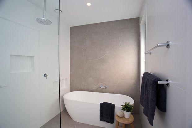Contemporary bathroom featuring a freestanding white bathtub, walk-in glass shower, large-format taupe stone-look wall and floor tiles, white walls, recessed lighting, and minimalist chrome towel rails and fixtures.