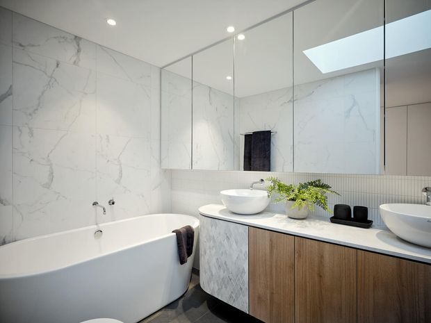 Bright contemporary bathroom featuring a freestanding white bathtub, double vessel basins on a timber vanity, large mirrored wall cabinets, white marble-look wall surfaces, fine vertical tile detailing, dark floor tiles, and a skylight.