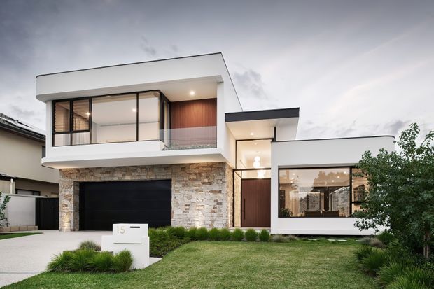 Contemporary two-storey residential facade with crisp white rendered volumes, extensive dark-framed glazing, a natural stacked-stone garage surround, warm timber accents, flat roof forms, and a landscaped front lawn.